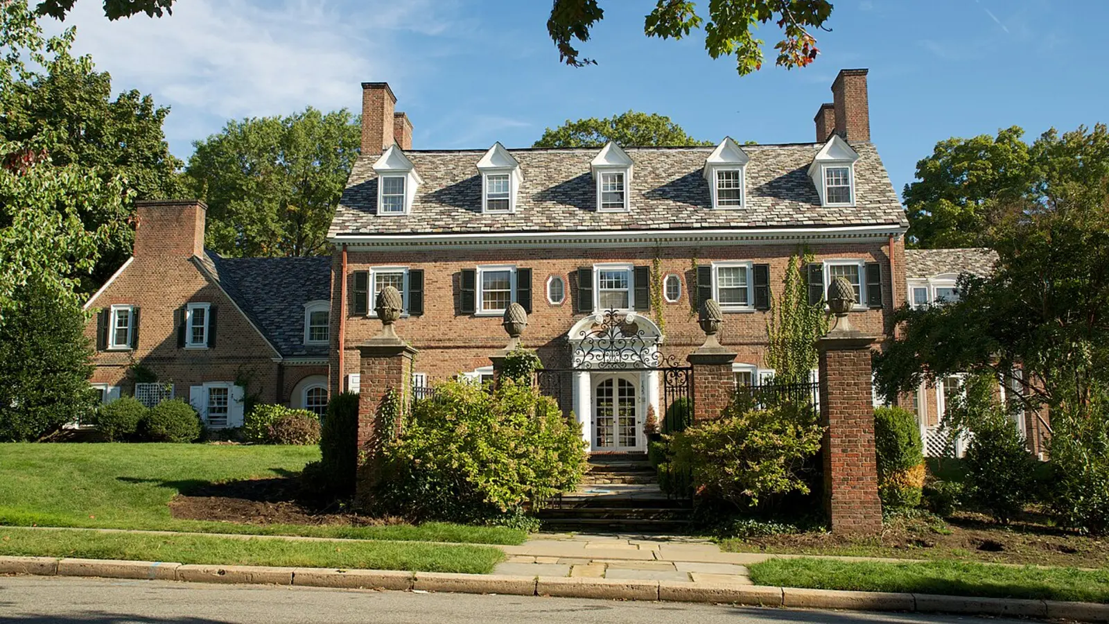 Older brick colonial-style house with neighboring homes and mature trees.